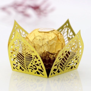 Intricate gold laser-cut leaf pattern candy wrapper with Ferrero Rocher on reflective surface