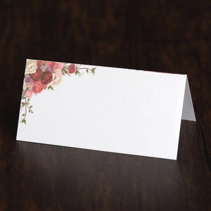 Detail of floral printed wedding place card on dark wood table with textured paper