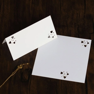 Detalle del diseño de corazón cortado por láser en tarjetas blancas de boda sobre madera