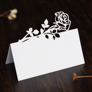 Detail of laser-cut white rose place card on dark wood table for wedding seating