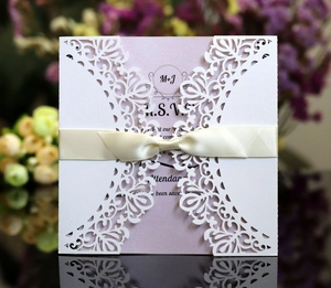 Close-up of laser-cut wedding invitation with white lace pattern and silk ribbon bow