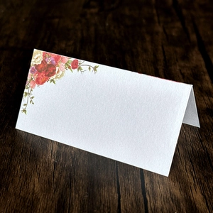 Detail of white floral place card with colorful rose printing on a dark wood table