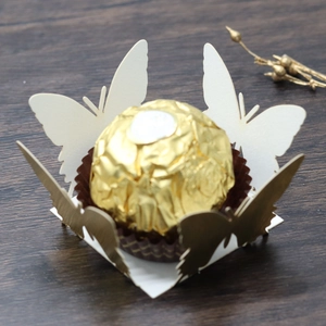 Detailed laser-cut white butterfly paper favor box for chocolate on a wooden background