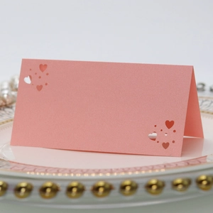Detalle de tarjetas de mesa rosa perlado con diseño de corazón calado en un plato