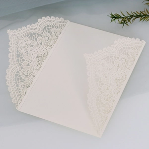 Detail of laser-cut cream wedding invitation with intricate lace patterns and floral design