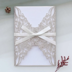 Détail de l'invitation découpée au laser avec paillettes et élégant nœud en ruban blanc