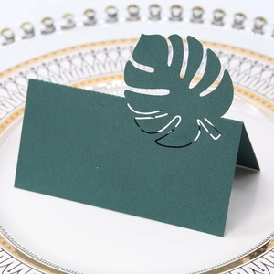 Détail du marque-place feuille de monstera vert foncé avec découpe laser sur assiette blanche