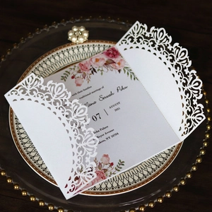 Close-up of laser-cut wedding invitation card with pink floral insert on a vintage plate