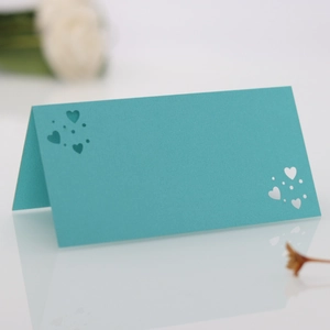 Detalle de tarjeta de mesa para boda verde azulado con corazones cortados por láser