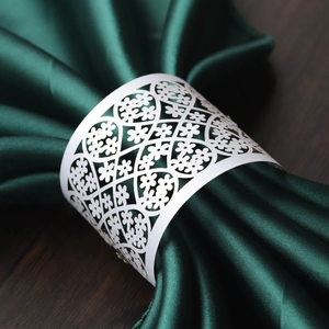White laser-cut floral paper napkin rings on dark green satin fabric for wedding table decor