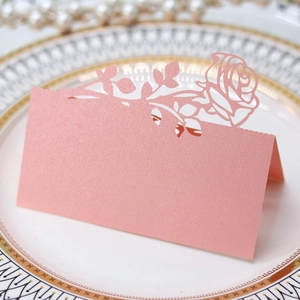 Detailed laser-cut pink rose table card on white plate for wedding reception setup