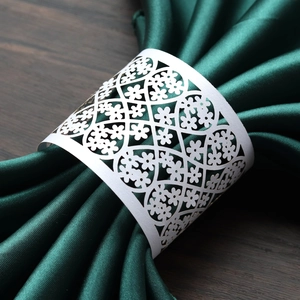 Detail of laser-cut floral napkin ring in white paper on a dark green silk napkin