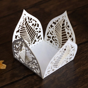 Macro shot of white pearlescent paper favor box with laser-cut leaf patterns