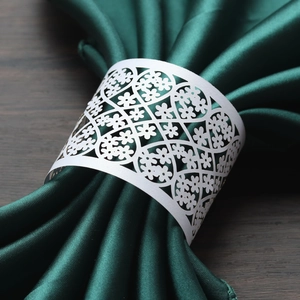 Close-up of laser-cut floral paper napkin rings on dark green velvet napkins for weddings