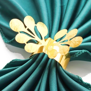 Elegant gold hollow leaf napkin ring with metallic luster on dark green silk backdrop