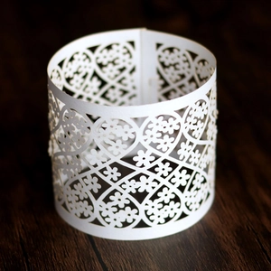 Close-up of white laser-cut paper napkin ring with floral and heart lace patterns