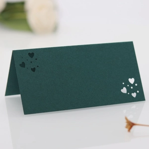 Detalle de tarjeta de mesa verde oscuro cortada con láser con corazones para bodas
