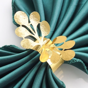 Macro detail of a golden leaf napkin ring on a luxurious dark green silk fabric