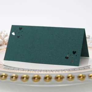 Detalle de tarjeta de mesa verde oscuro con corazones cortados a láser en plato blanco