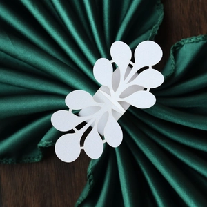 Detailed view of white laser-cut leaf napkin ring on dark green satin fabric