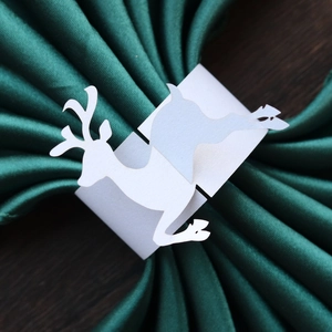 Close-up of white reindeer paper napkin ring on green satin fabric over wooden table