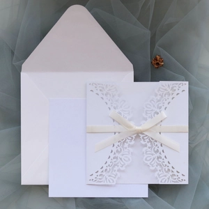 Detailed laser-cut wedding invitation set with white ribbon bow on mesh background
