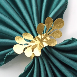 Macro shot of gold leaf napkin ring with hollow design on dark green satin fabric