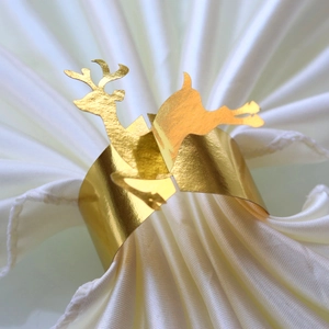 Detail of mirror gold reindeer napkin ring on a white satin napkin for Christmas decor