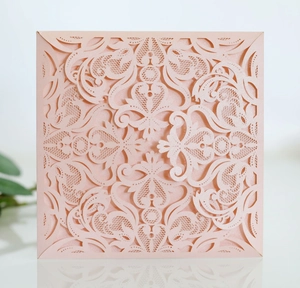 Macro detail of laser-cut floral lace pattern on pale pink wedding invitation card