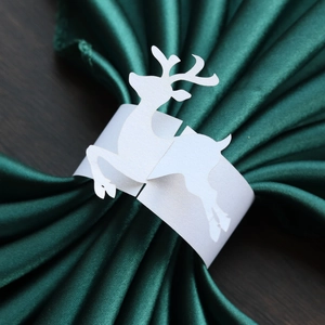 Close-up of laser-cut white reindeer paper napkin ring on a dark green fabric napkin
