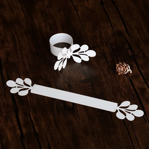 Detailed laser-cut white napkin ring with intricate leaf patterns on a wooden surface