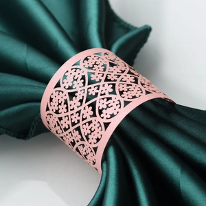 Pink laser-cut floral paper napkin ring on a dark green satin cloth for wedding decor