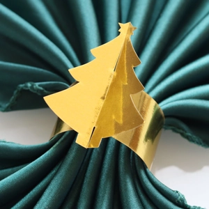 Gros plan du rond de serviette sapin de Noël doré sur une serviette en soie vert foncé chic