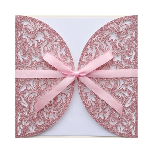 Détail d'un faire-part de mariage ajouré rose pailleté avec un élégant nœud en ruban