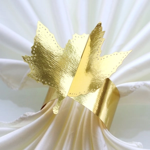 Macro detail of a golden maple leaf paper napkin ring on a white silk napkin