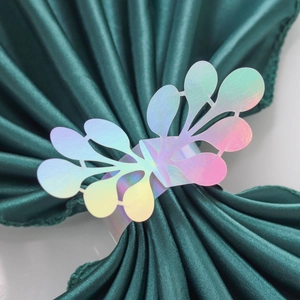 Macro detail of iridescent paper napkin rings with floral cutouts on green satin