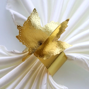 Detail of a golden maple leaf napkin ring with intricate laser-cut dots on white fabric