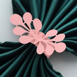Macro detail of pink laser-cut pearl paper napkin ring on a dark green satin fabric