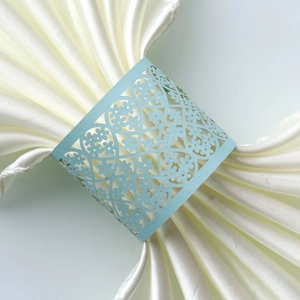 Detail of light blue laser-cut paper napkin ring with floral lace pattern on white satin
