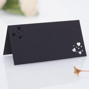 Detalle de tarjetas de mesa negras mate con corazones cortados por láser y fondo floral suave