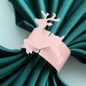 Close-up of pink reindeer paper napkin ring with pearlescent texture on green silk fabric
