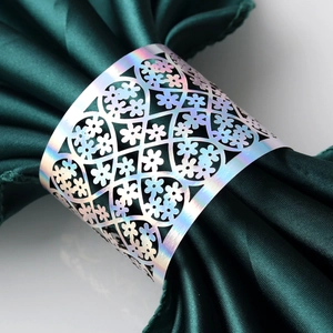 Detail of laser-cut silver napkin ring with floral hollow pattern on dark green fabric