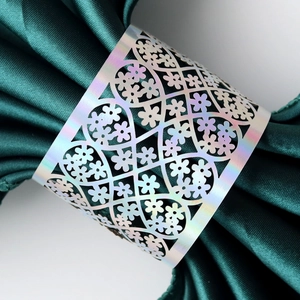Detail of laser-cut floral pattern napkin ring with iridescent silver finish on green fabric