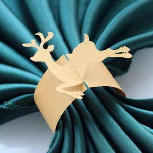 Macro shot of golden reindeer paper napkin ring on a dark green satin cloth for Christmas