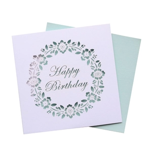 Detail of laser-cut floral wreath design on white birthday card with green metallic text
