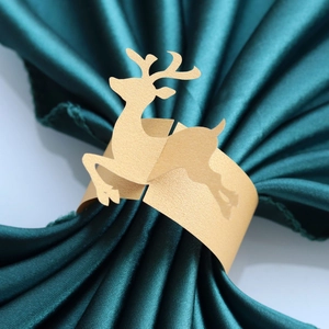 Close-up of golden reindeer paper napkin ring on green satin fabric for Christmas