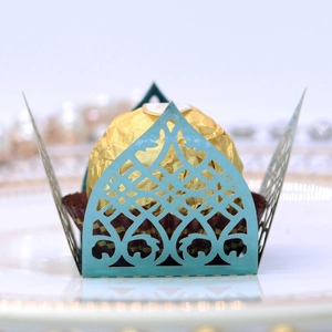 Detail of laser-cut teal candy box with intricate crown pattern holding a chocolate