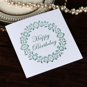 Elegant laser-cut pearl white Happy Birthday card with intricate floral wreath on wood