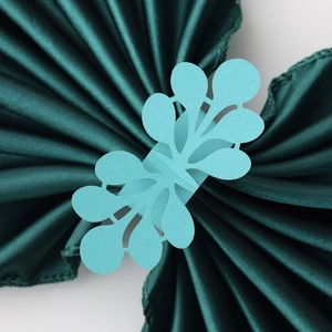 Detail of light blue laser-cut floral paper napkin ring on dark green satin fabric