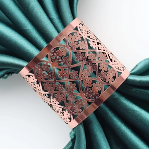 Macro detail of rose gold napkin ring featuring intricate hollowed flower patterns on satin
